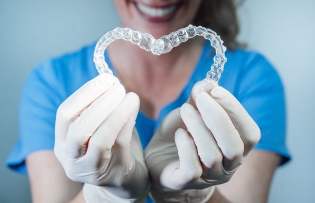 cosmetic dentist in West Edmonton holding two Invisalign aligners in the shape of a heart