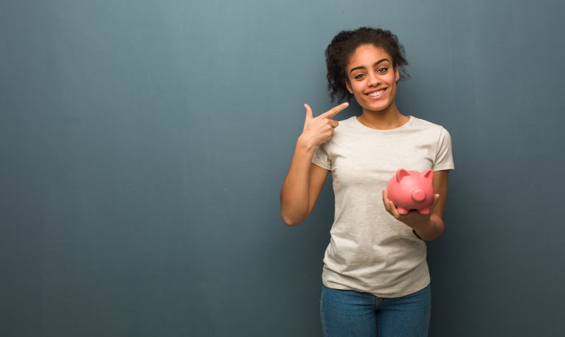 woman with Invisalign in West Edmonton holding a piggy bank and pointing to her smile