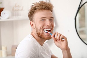 man brushing teeth for dental implant care in Edmonton