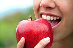 Closeup of patient with dental implants in Edmonton eating an apple